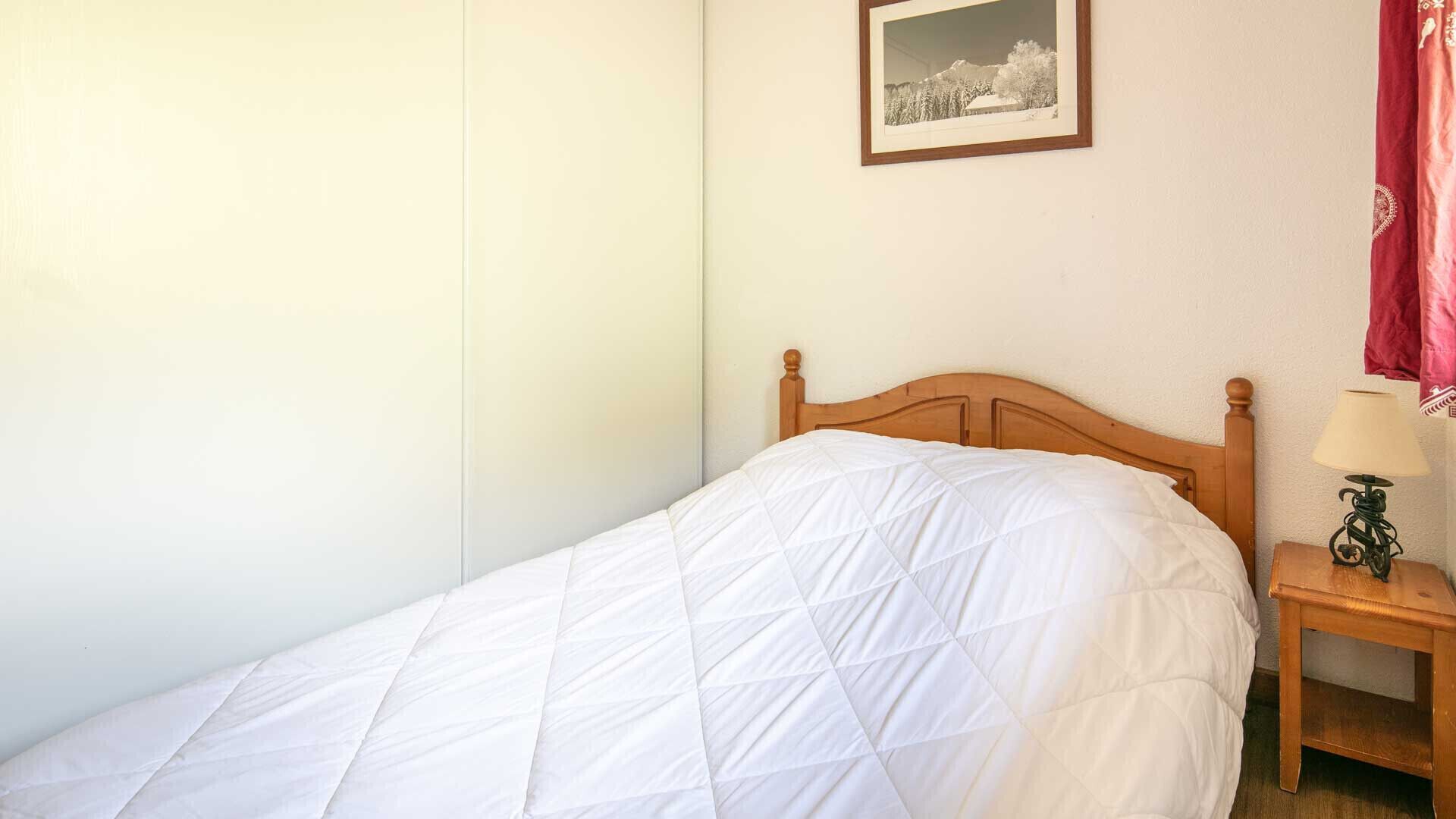 A single bed with a wooden headboard, a bedside table with a lamp, and a framed picture on the wall.