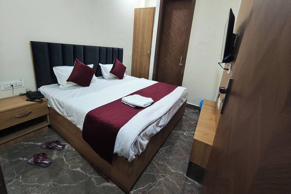 A neatly made bed with a dark headboard, a wooden nightstand with a phone, and a pair of slippers on the floor.