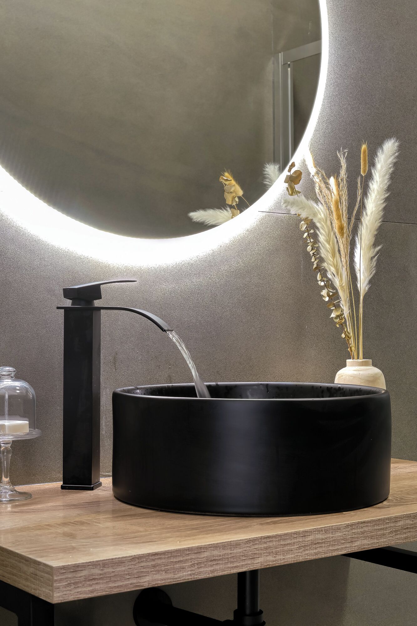 Une salle de bain moderne avec un lavabo rond noir, un robinet et un vase contenant de l’herbe des pampas.