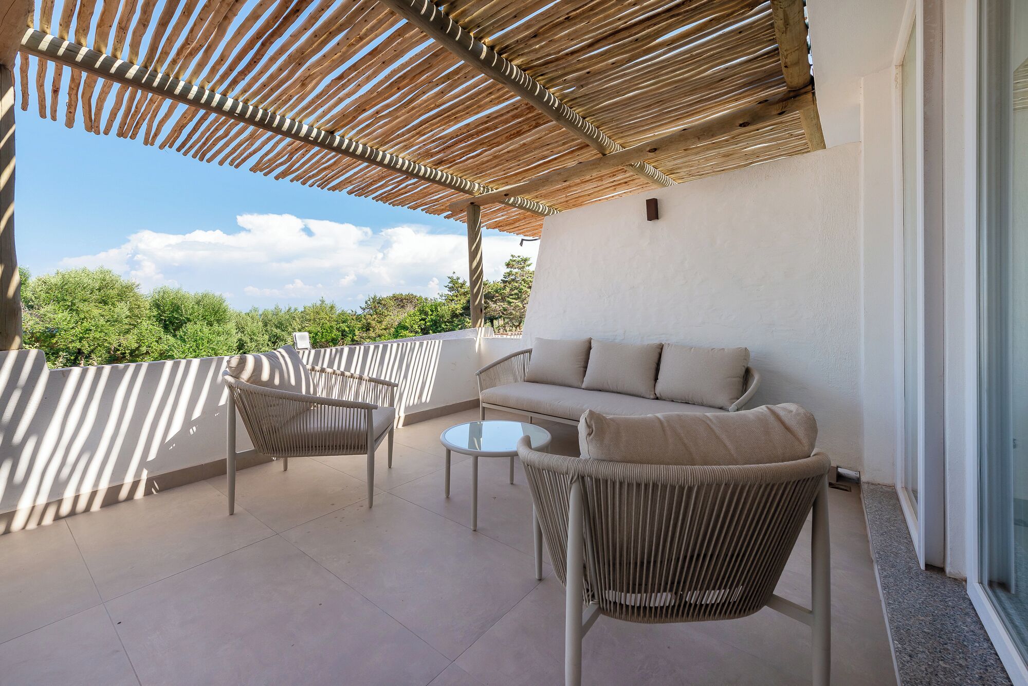 Ein Balkon mit gewebtem Dach, einer Couch, zwei Stühlen und einem kleinen Tisch.