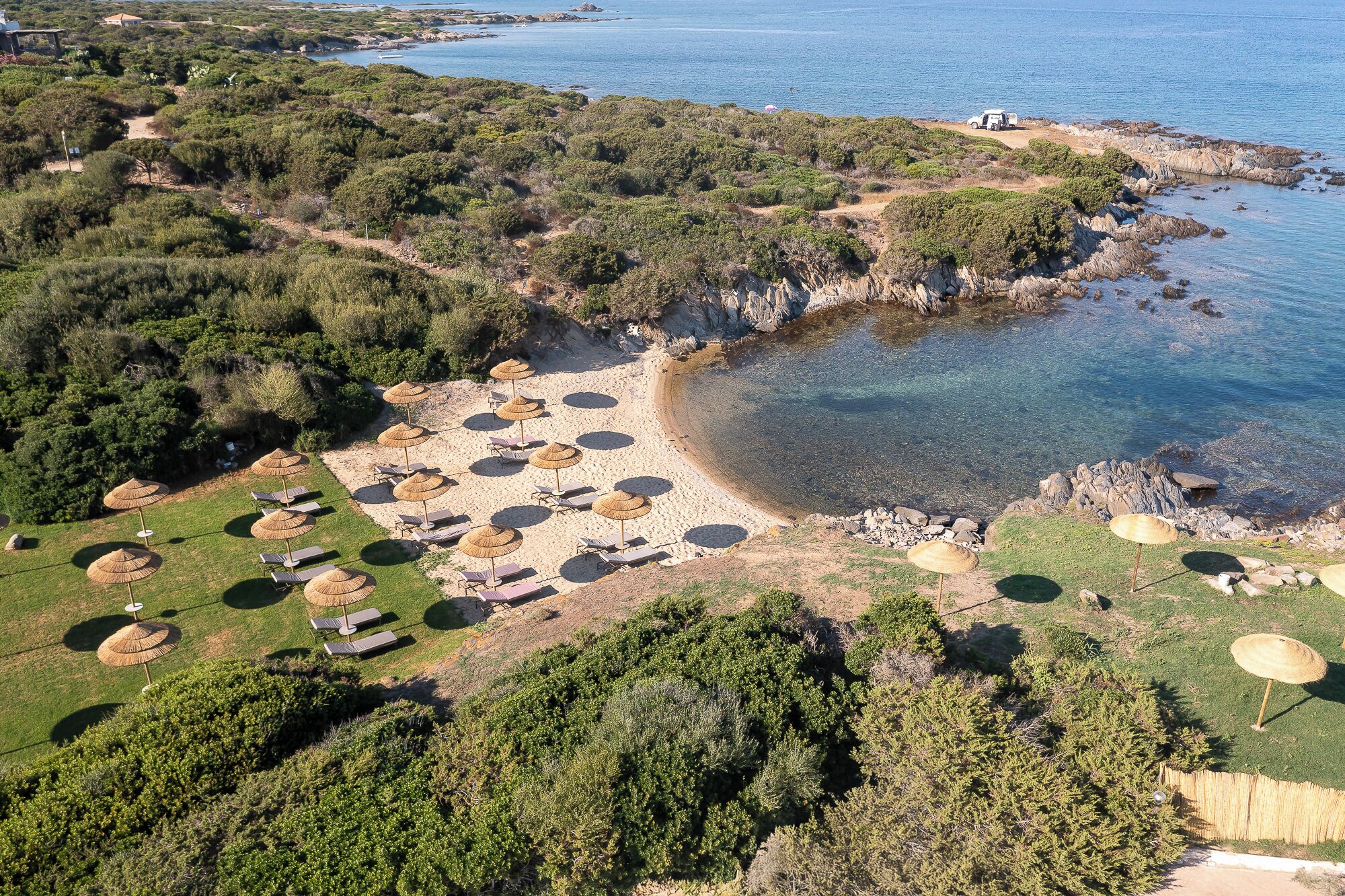 An aerial view of a coastal area with a beach, umbrellas, and lounge chairs.