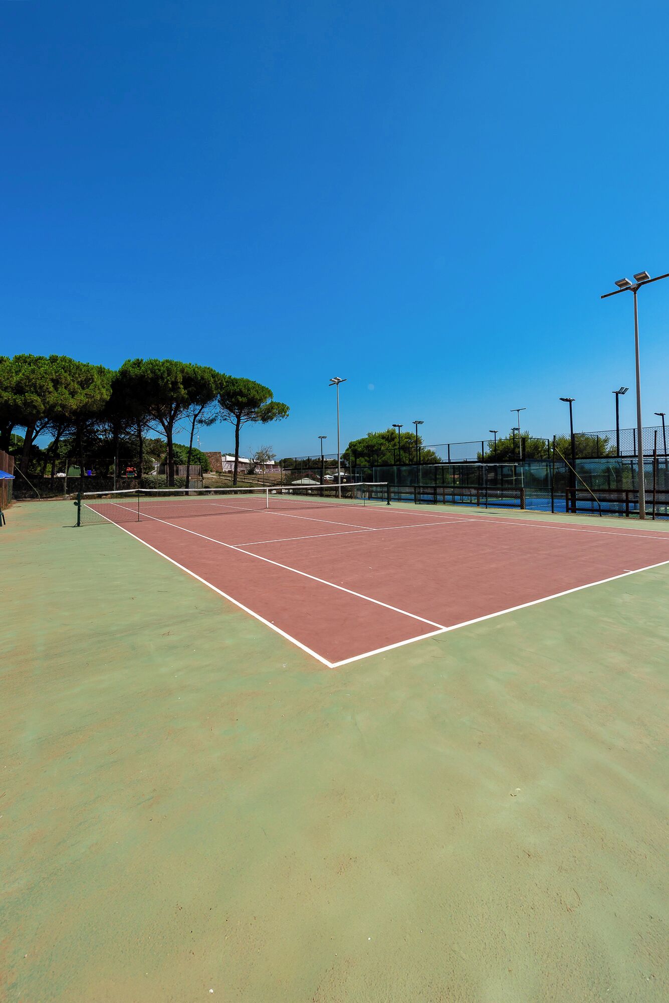 An outdoor tennis court with a net, surrounded by trees and a fence.