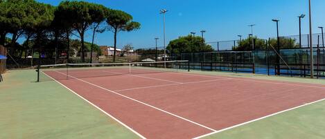 Cancha de tenis al aire libre con red, rodeada de árboles y una valla.