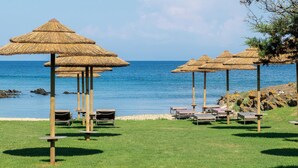A beachside area with thatched umbrellas and lounge chairs, a clear view of the sea, and a rocky shoreline. - Cala Lupo Resort (Stintino)