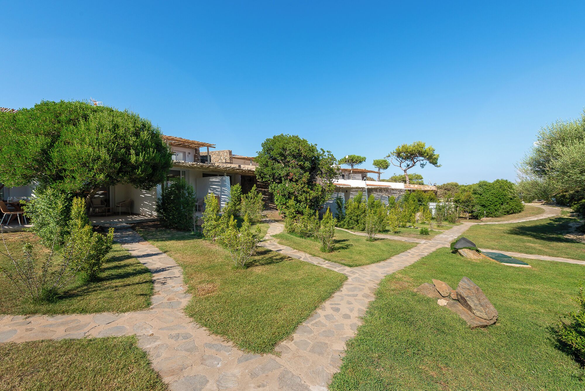 A pathway leading to a building with a stone facade and a tiled roof, surrounded by greenery and trees.