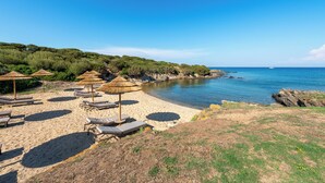 A beach with sun loungers, umbrellas, and a rocky coastline. - Cala Lupo Resort (Stintino)