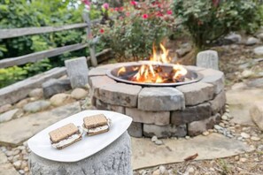 Un foyer en pierre avec deux chamallows grillés sur une assiette blanche, le tout installé dans un jardin.