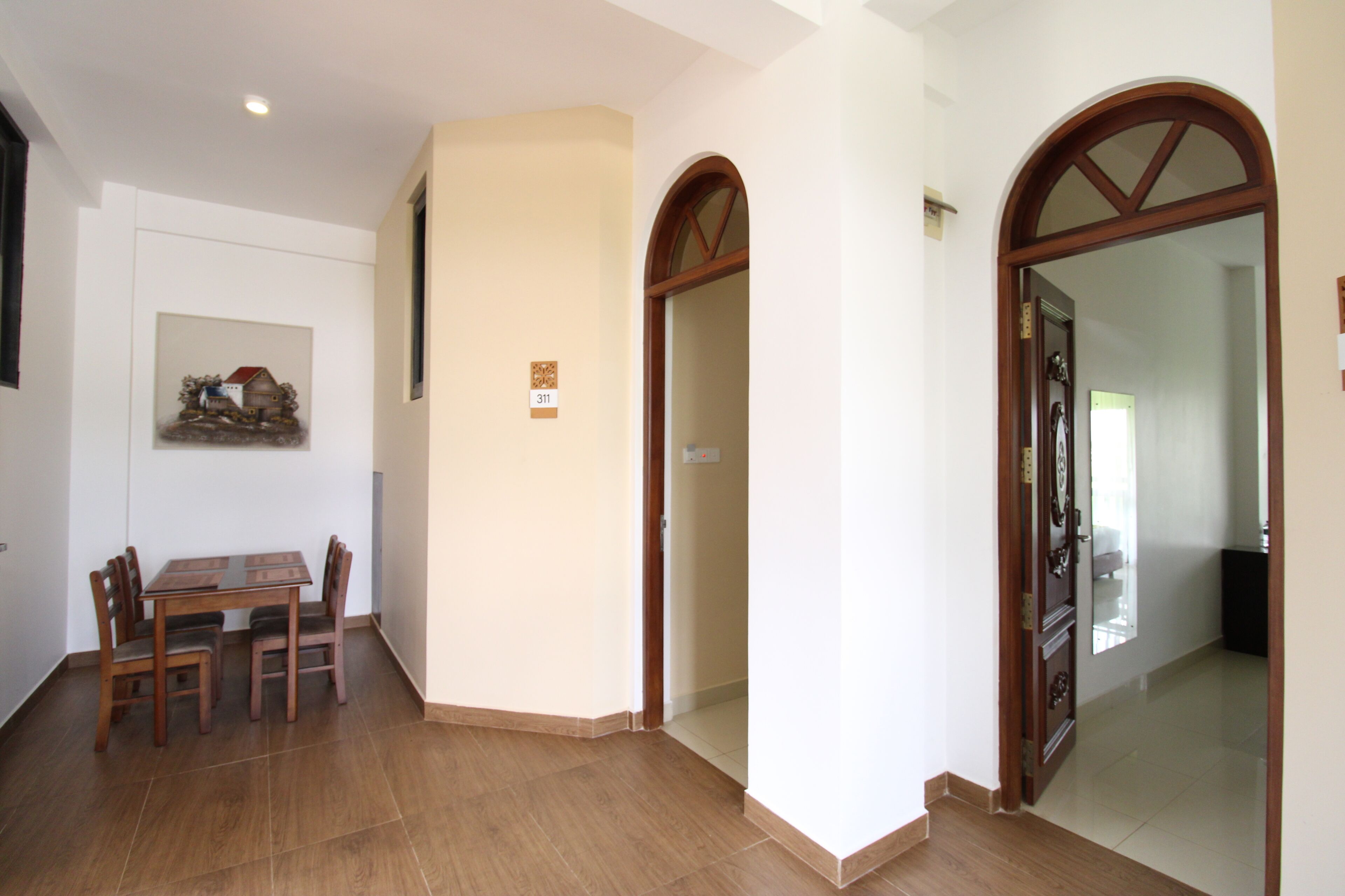 A dining area with a wooden table and chairs, a wall-mounted picture, and a door leading to another room.