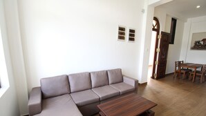 A living room with a sectional sofa, a wooden coffee table, and a dining area with chairs. - Kynrock Hotels & Resorts (Kataragama)