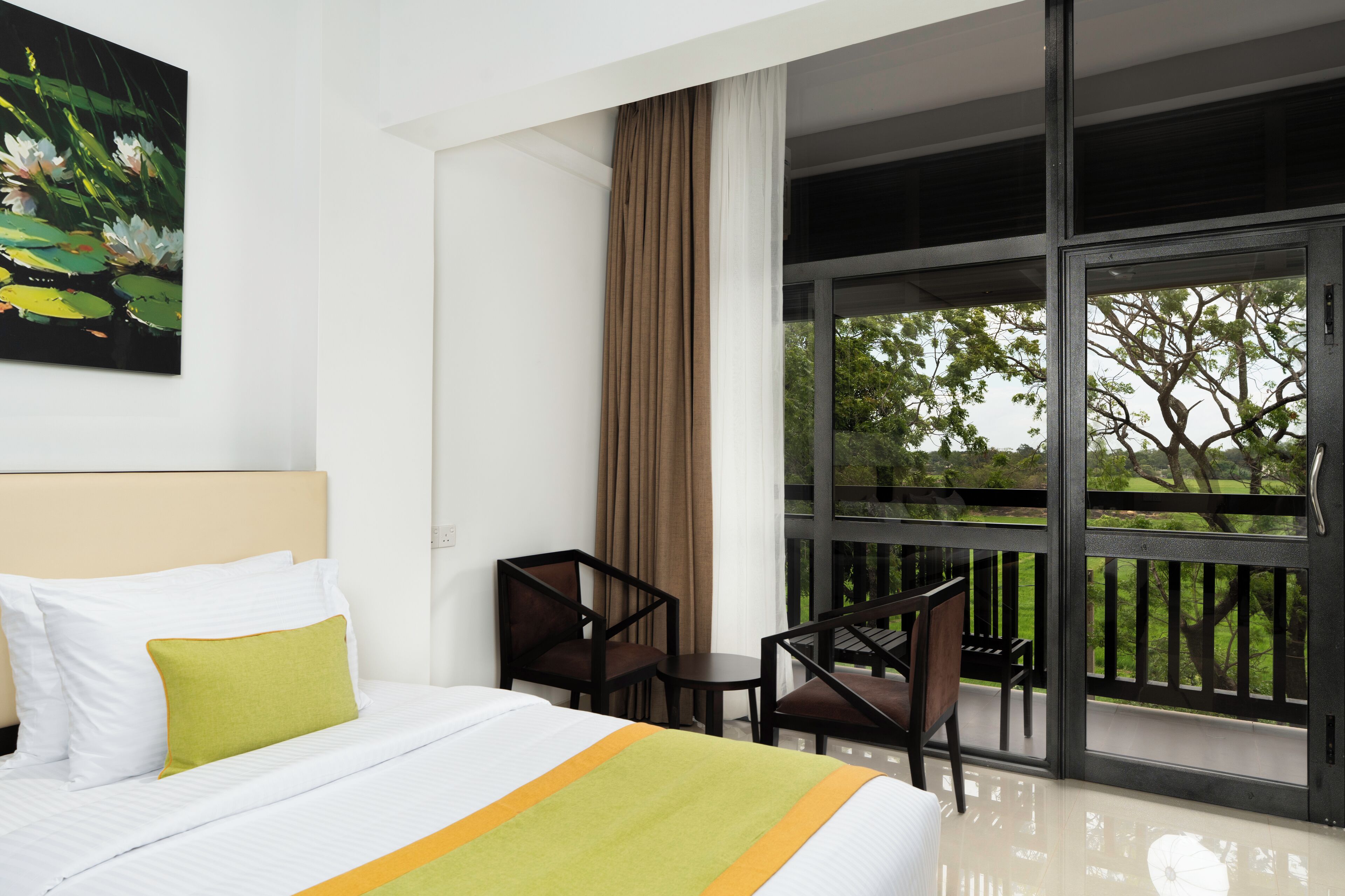 Habitación de hotel con cama, una silla, una mesa y un ventanal con vistas a zonas verdes.