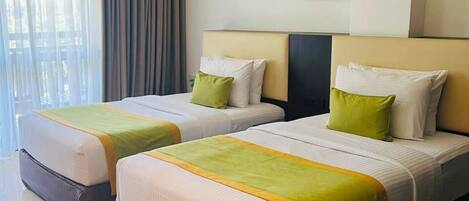 A hotel room with two beds, a large window with curtains, a wall-mounted air conditioner, and a painting.