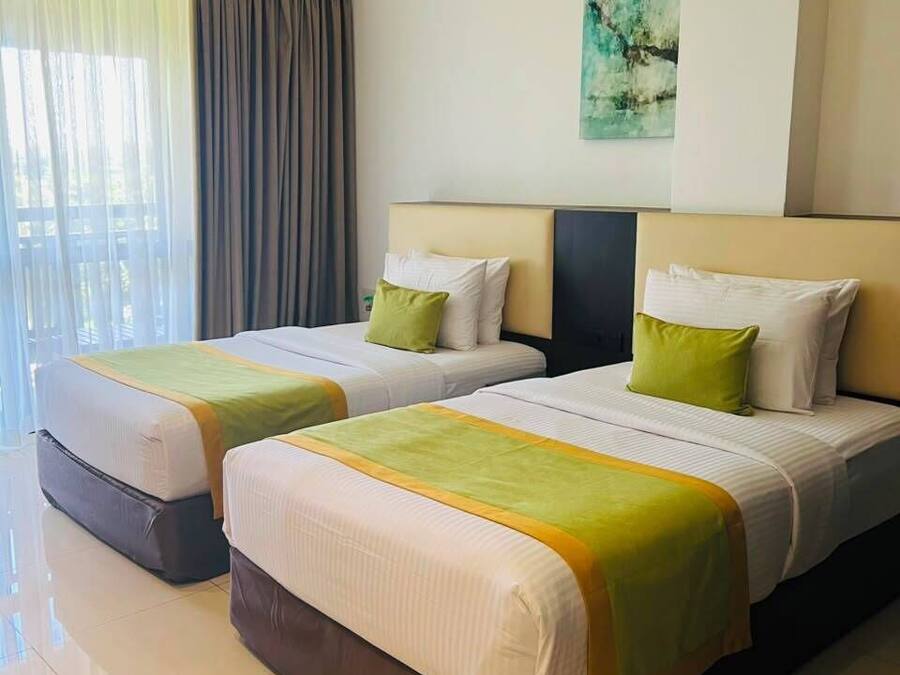 Habitación de hotel con dos camas, un ventanal con cortinas, aire acondicionado instalado en la pared y un cuadro.