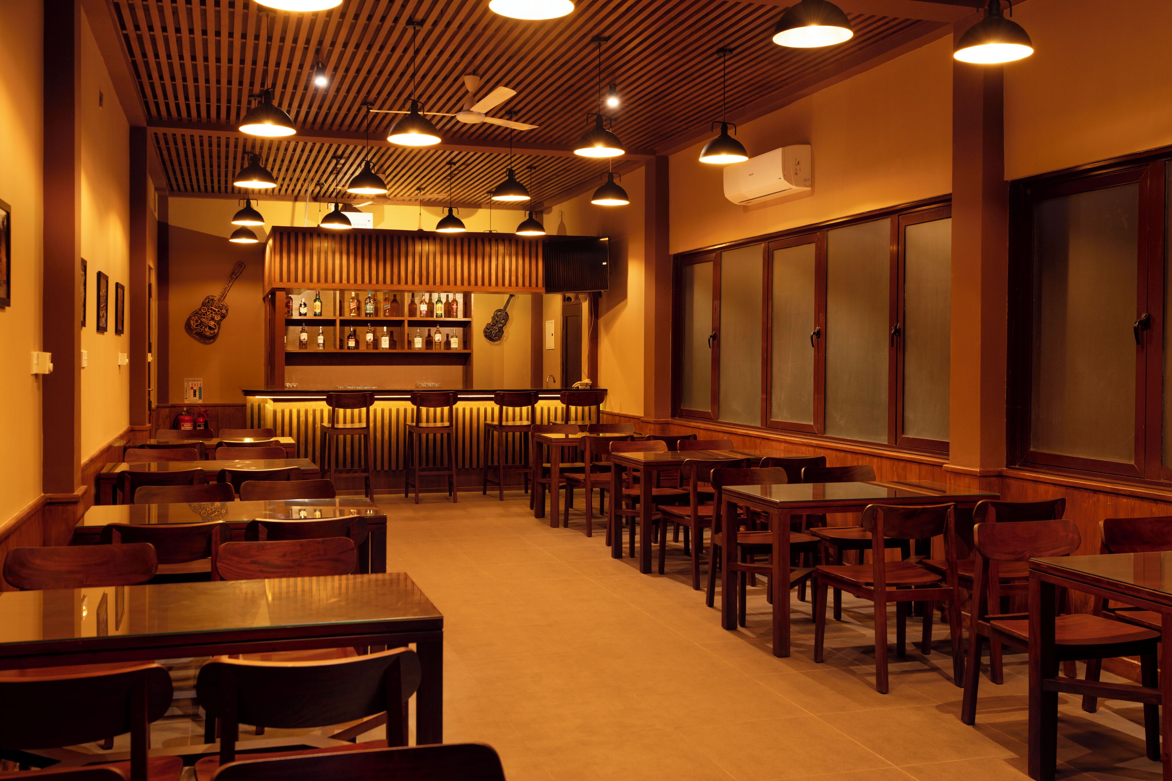 A restaurant with wooden ceiling, multiple tables and chairs, a bar area, and a large window.