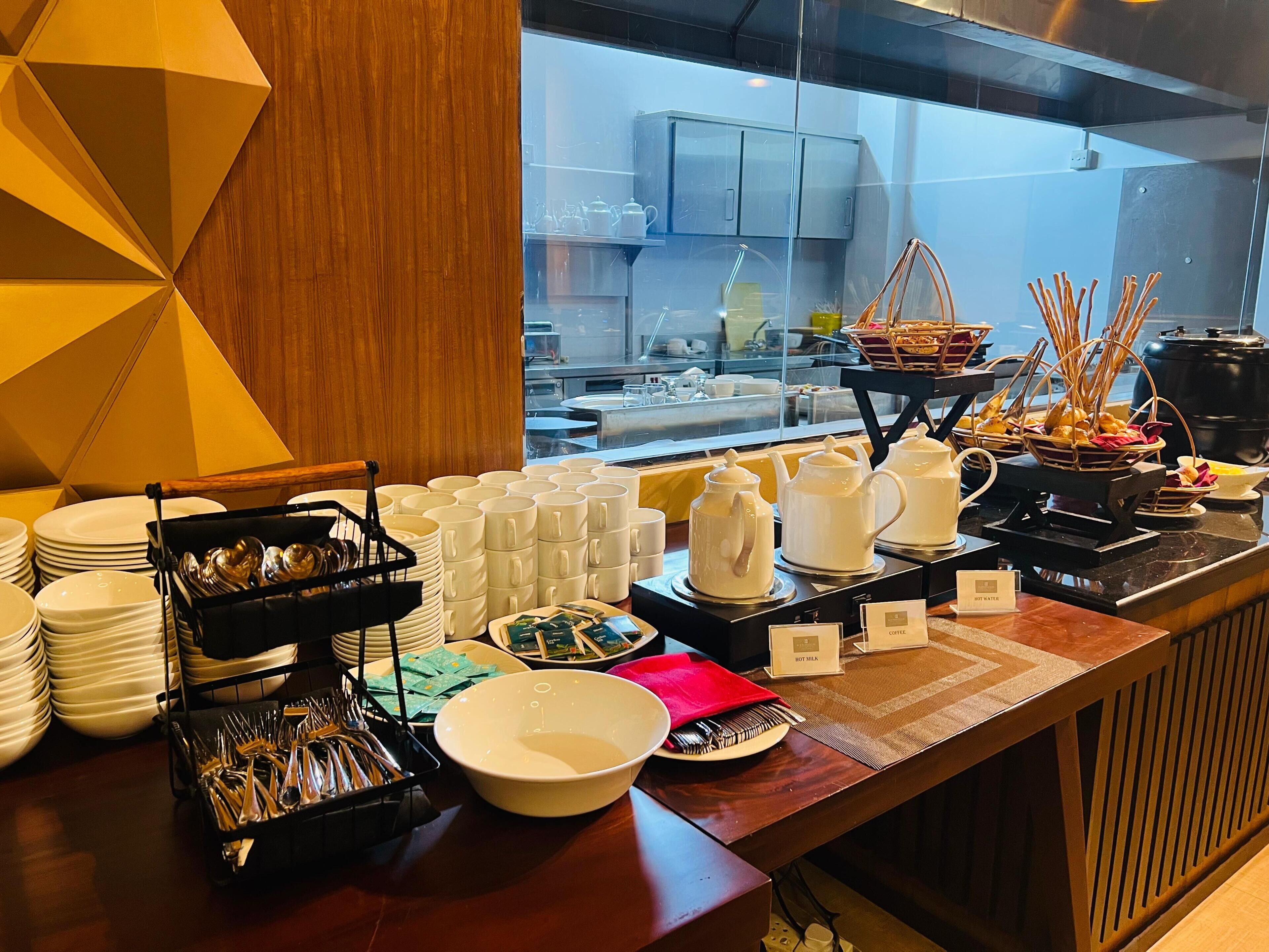 A buffet setup with stacked plates, bowls, and teapots, and a window view of the kitchen area.