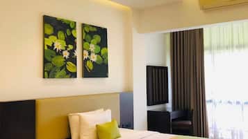 Habitación de hotel con cama, mesita de noche, ventilador de techo, obras de arte y una ventana con cortinas.