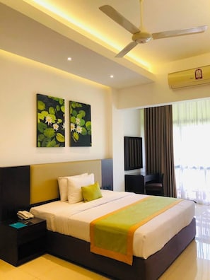 A hotel room with a bed, bedside table, ceiling fan, artwork, and a window with curtains. - Kynrock Hotels & Resorts (Kataragama)