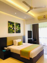 Habitación de hotel con cama, mesita de noche, ventilador de techo, obras de arte y una ventana con cortinas.