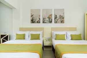 Habitación de hotel con dos camas, cada una con almohadas y una manta verde. Hay dos mesitas de noche, una con teléfono y otra con lámpara. Las paredes exhiben tres obras de arte botánicas.
