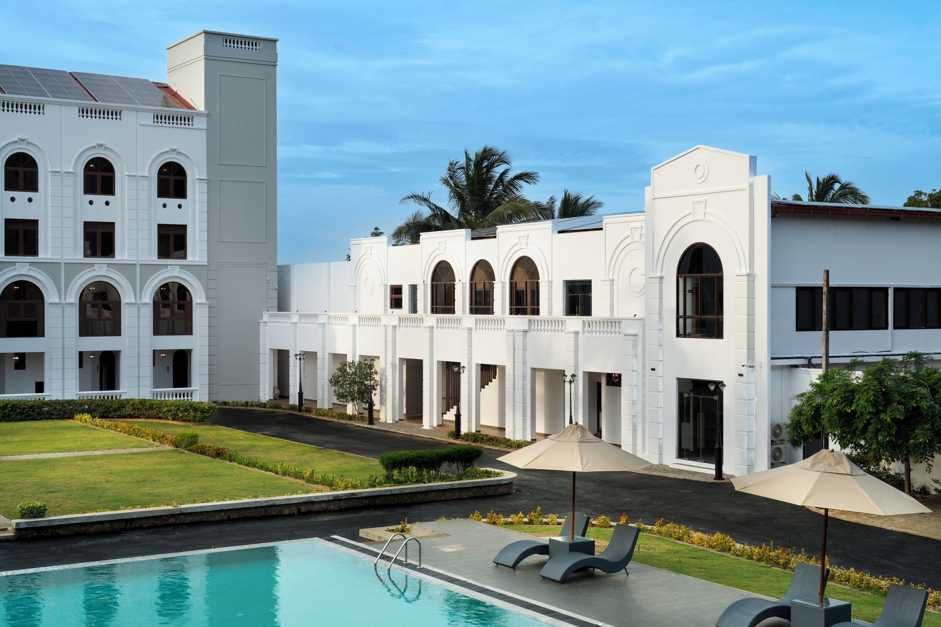 A hotel with a swimming pool, outdoor seating, and a well-maintained lawn.