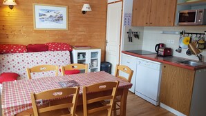A cozy kitchen with wooden cabinets, a dining table with chairs, and a microwave. - Lovely 5-pers ground floor apt with terrace (Chamrousse)