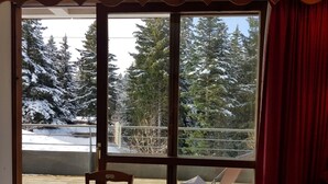 A room with a wooden table and chairs, a sliding glass door leading to a balcony with a view of snow-covered trees and a fence. - Lovely 5-pers ground floor apt with terrace (Chamrousse)