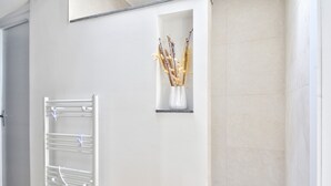 A bathroom with a white bathtub, a wooden bench, a towel rack, and a vase with dried flowers.
