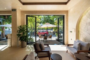 Un vestíbulo moderno con un sofá, sillas, una planta en maceta y vistas a una zona exterior con sombrillas.
