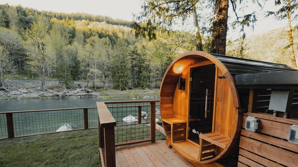 Eine Holzhütte mit rundem Innenraum, einer Terrasse und Blick auf Fluss und Wald.