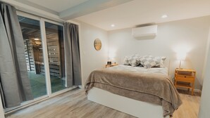 Ein Schlafzimmer mit einem Bett, einem Nachttisch, einer Lampe, einer Klimaanlage und einer Schiebeglastür.