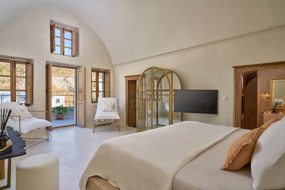 Un dormitorio amplio con una cama grande, un televisor montado en la pared y un balcón con una silla y una planta en maceta.