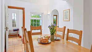Et spiseområde med et træbord, stole, en vase med blomster og en tallerken med croissanter.