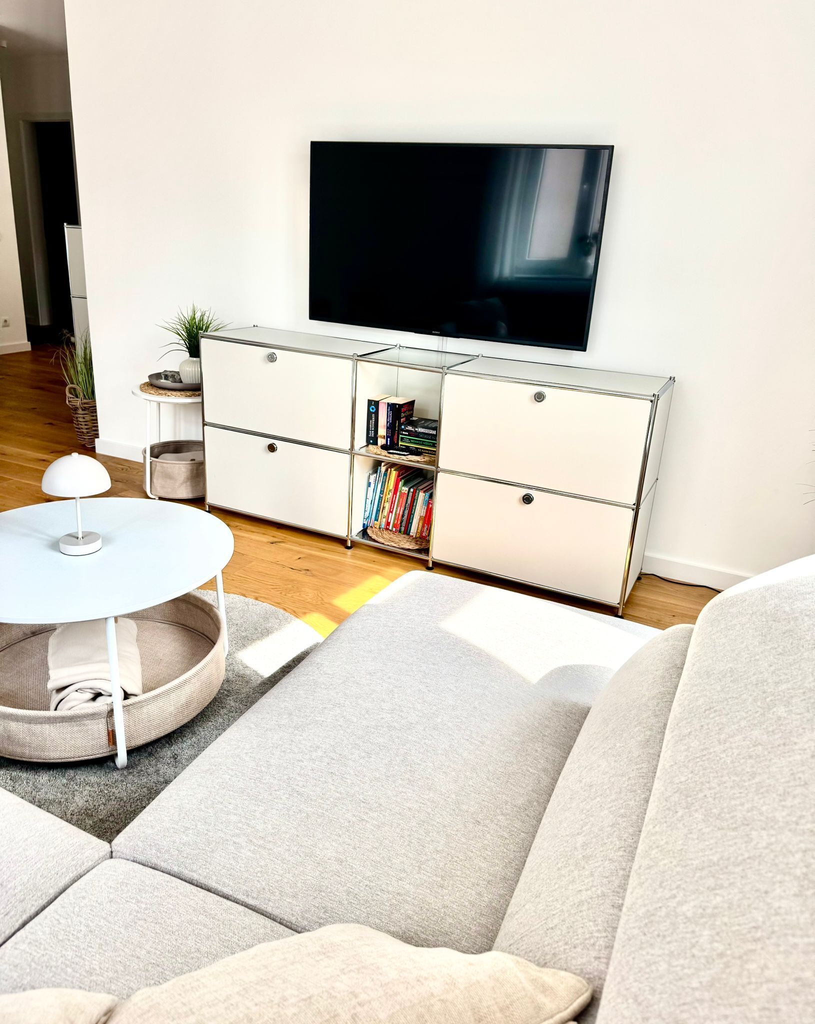 Ein modernes Wohnzimmer mit einer Couch, einem runden Couchtisch, einem weißen Schrank mit Büchern und einem Flachbildfernseher an der Wand.