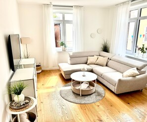 Un salon moderne avec un canapé d’angle, une petite table ronde et un téléviseur posé sur un meuble.