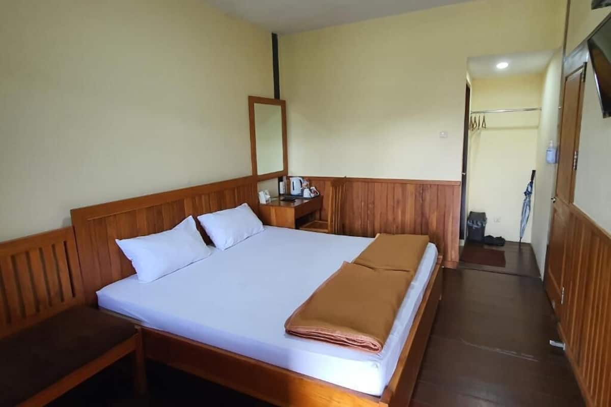 Ein Einzelbett mit Holz-Kopf- und Fußteil, ein Nachttisch mit Lampe und ein Spiegel an der Wand.