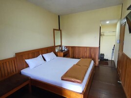Uma cama de solteiro com cabeceira e peseira de madeira, mesa de cabeceira com abajur e espelho na parede.
