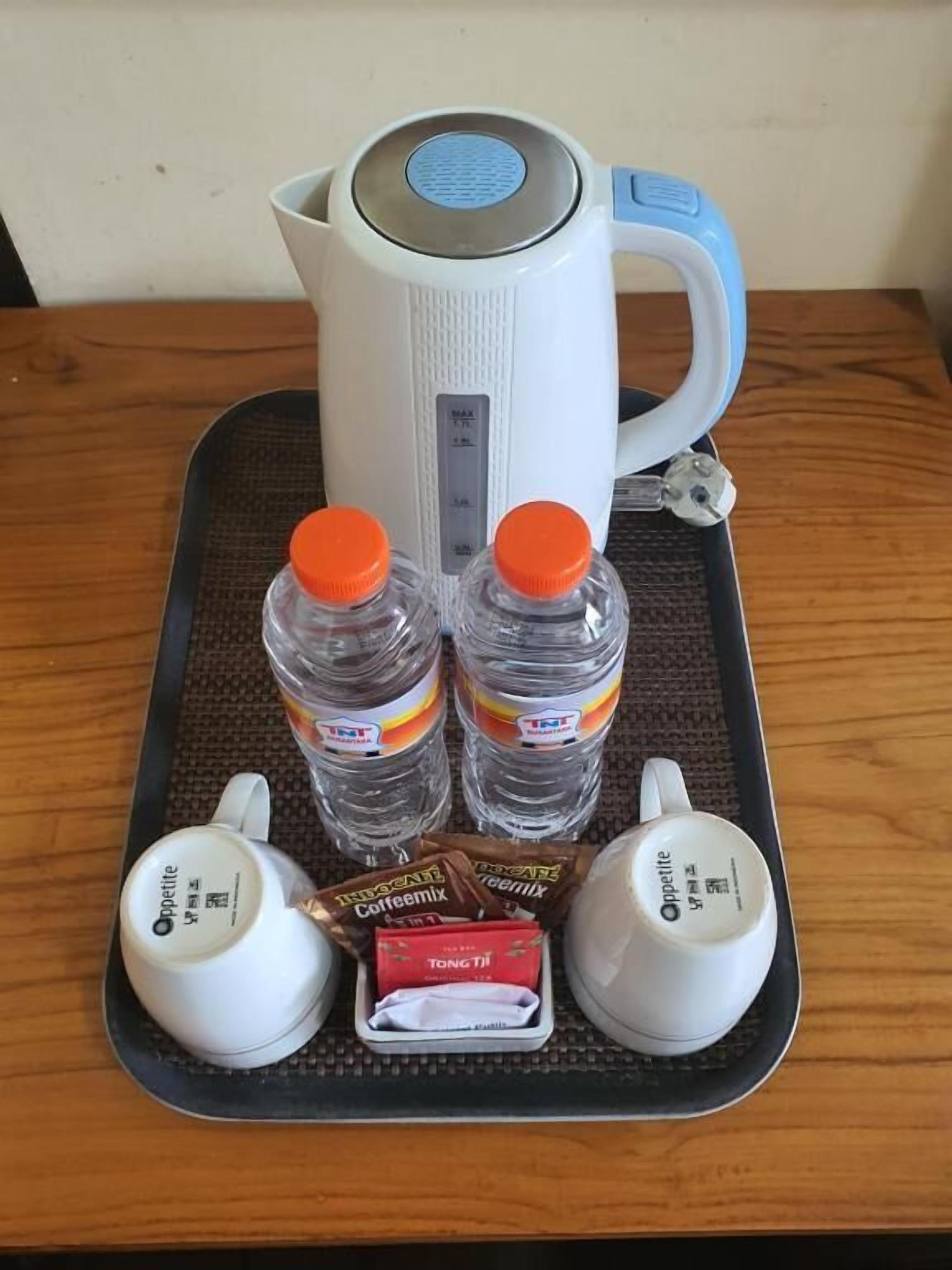 A tray with a kettle, two water bottles, two coffee cups, and a packet of coffee mix.