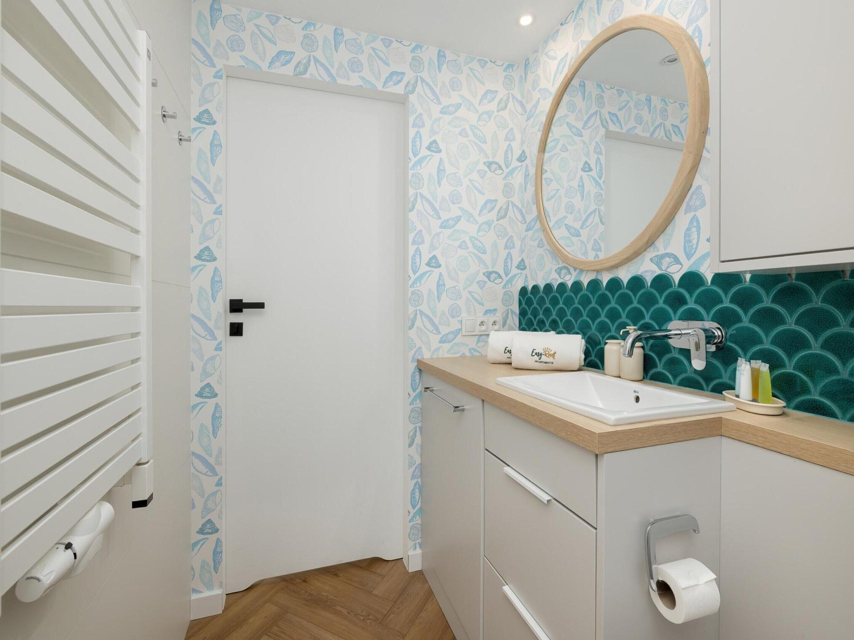 Un baño con una puerta blanca, un lavamanos con un espejo encima y un porta papel higiénico.