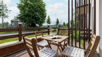 Un espacio de esparcimiento al aire libre con mobiliario de madera y cojines, con vistas a la vegetación y un edificio al fondo.