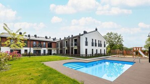 Un edificio residencial con piscina, césped y parque infantil.