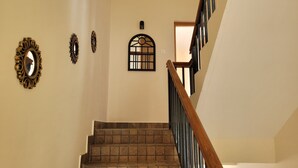 A staircase with a wooden handrail and a tiled floor, leading to a landing with a small window and wall-mounted decor. - The Ark Haven Ooty (Adikaratti)