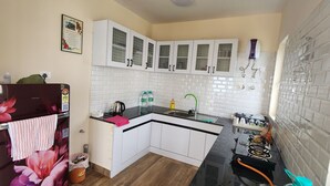 A compact kitchen with white cabinets, a black countertop, and a tiled backsplash. - The Ark Haven Ooty (Adikaratti)