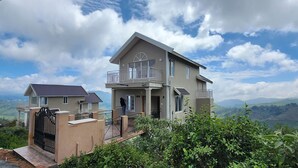 A two-story house with a balcony, surrounded by lush greenery and a mountainous landscape. - The Ark Haven Ooty (Adikaratti)