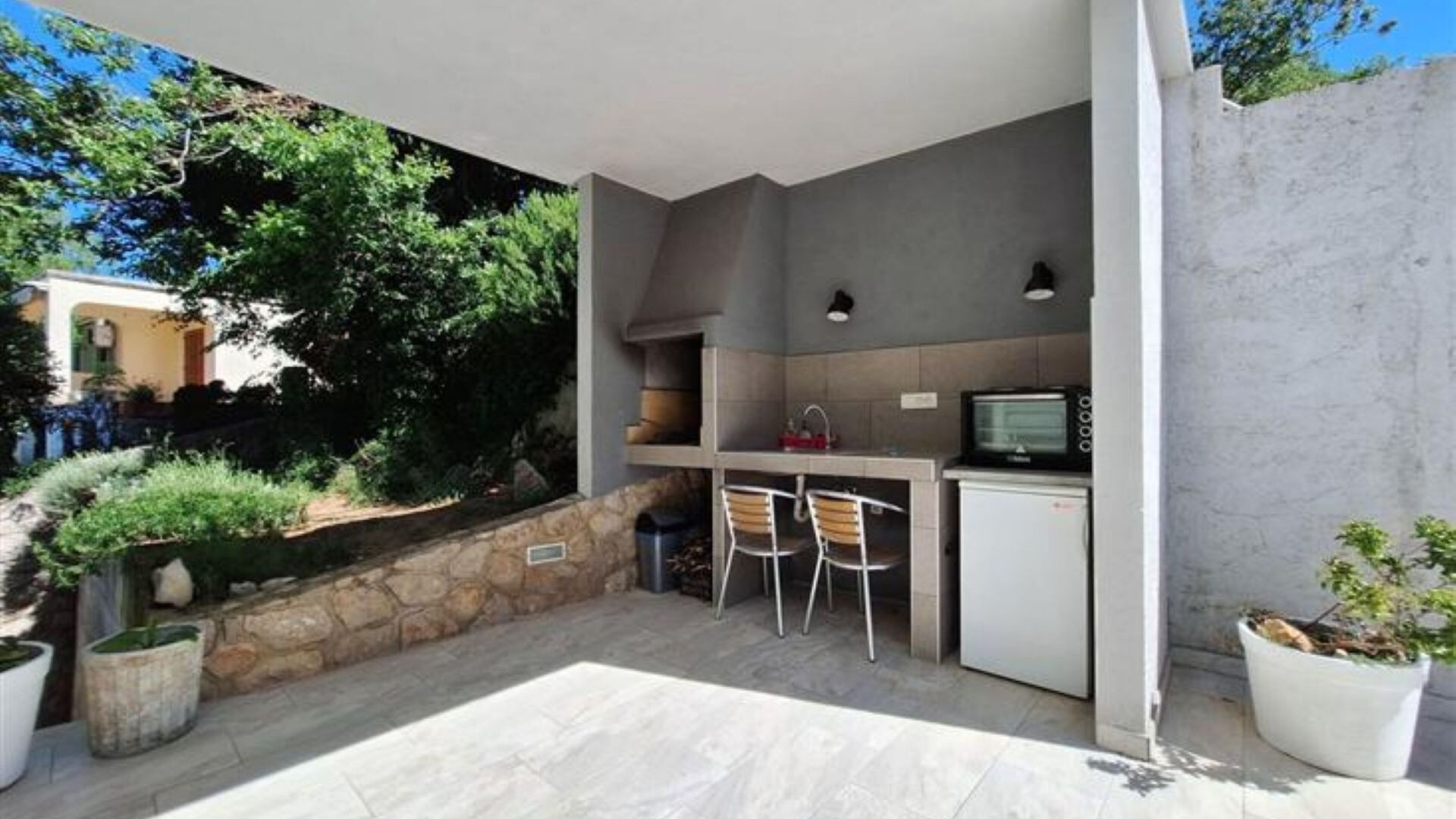 Un área de cocina al aire libre con pared de piedra, dos taburetes de bar, un microondas y un lavamanos.