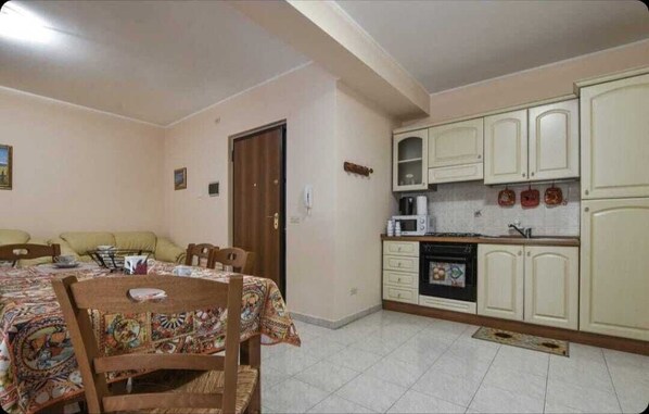 A compact kitchen with white cabinets, a microwave, and a stove. There is a dining area with a table and chairs, and a door leading to another room.