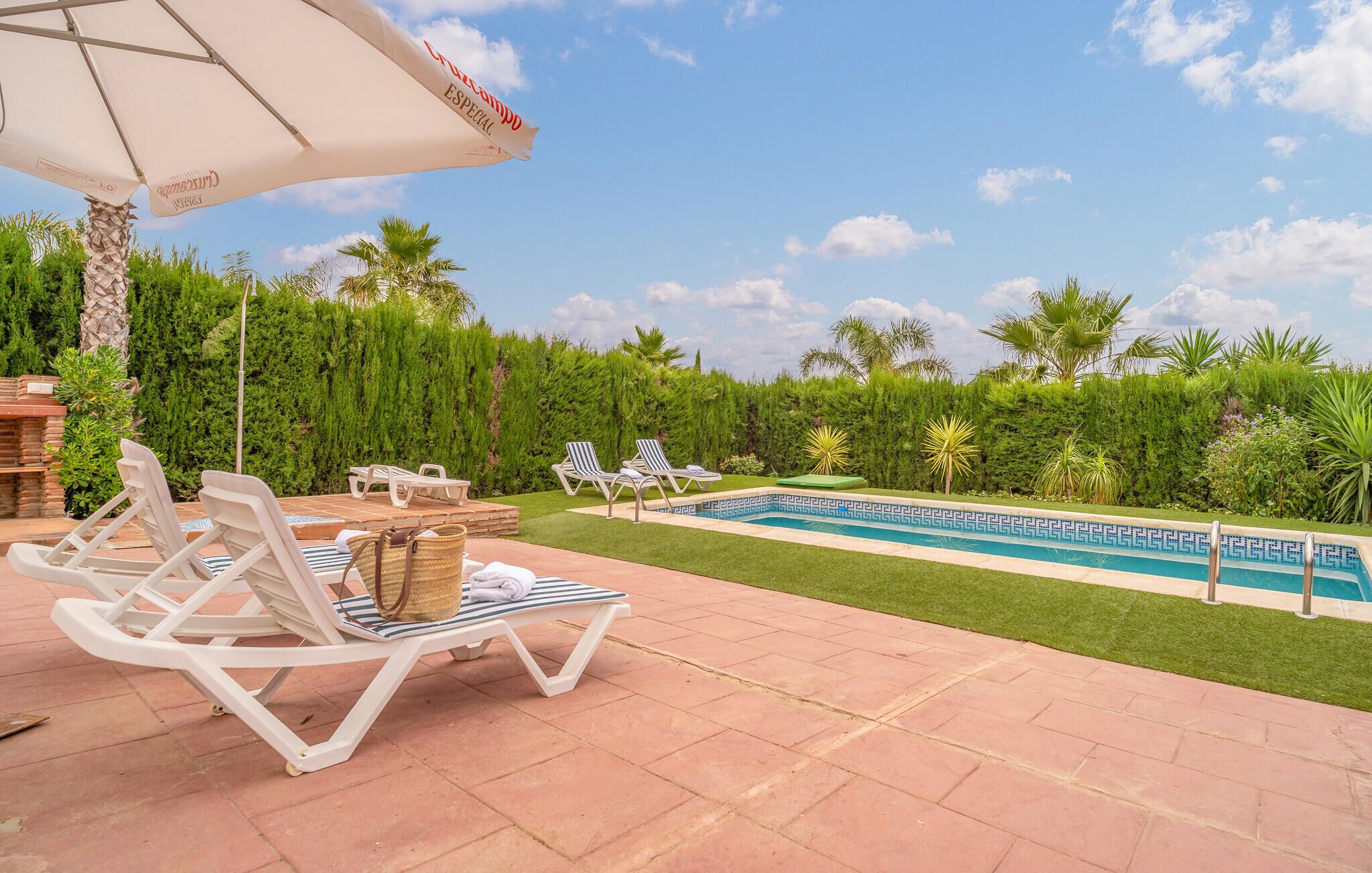 A poolside area with lounge chairs, a white umbrella, and a clear blue sky.