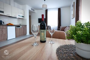 Eine moderne Küche mit einer Weinflasche und zwei Gläsern auf einem Holztisch, einer Topfpflanze und einer Couch im Hintergrund.