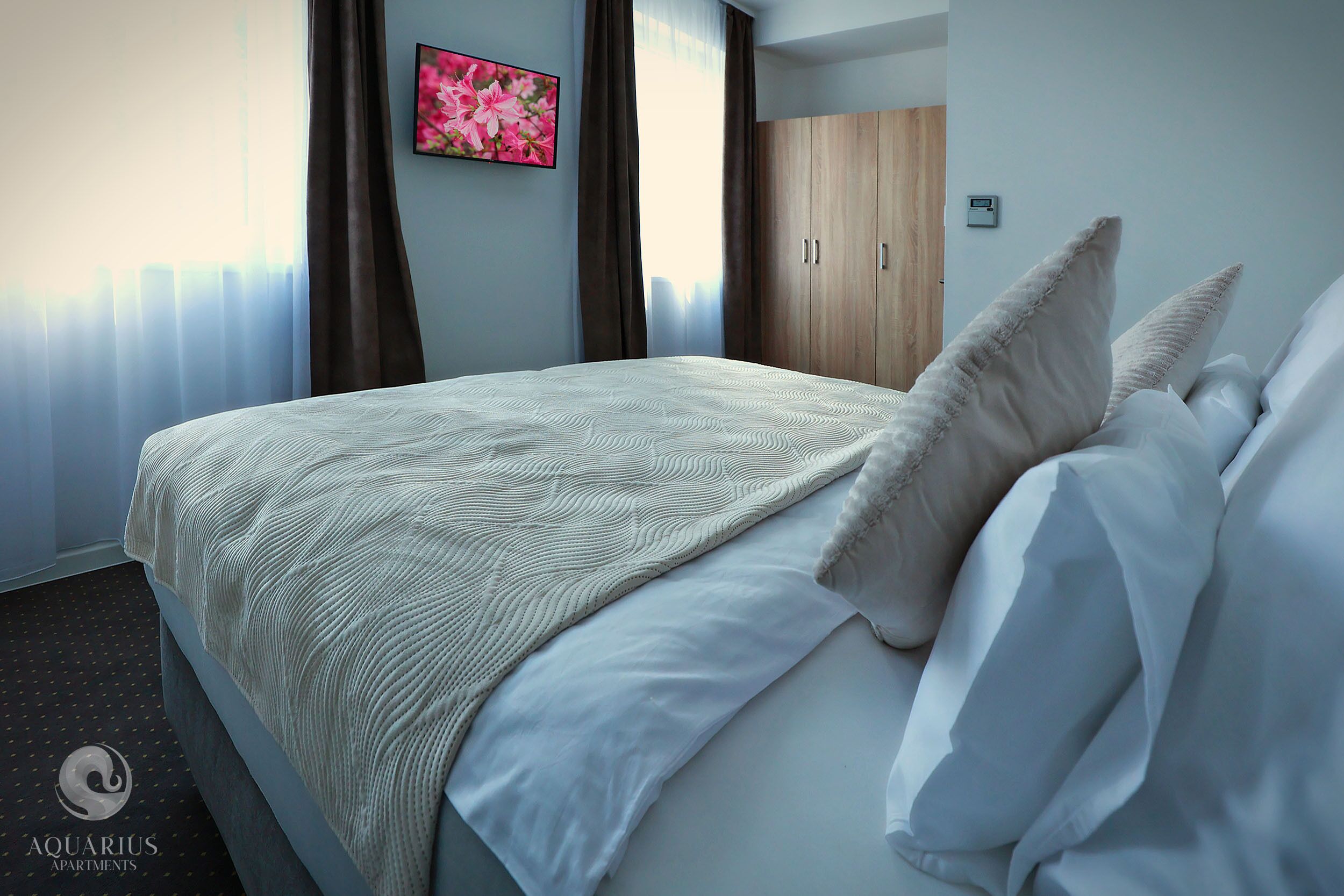 A neatly made bed with a patterned blanket and pillows, a wooden wardrobe, and a framed floral artwork on the wall.