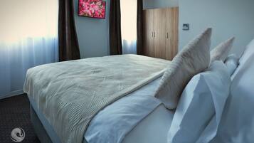 A neatly made bed with a patterned blanket and pillows, a wooden wardrobe, and a framed floral artwork on the wall.