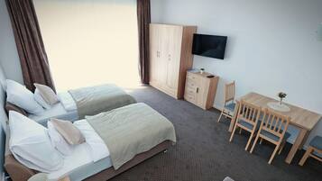 A hotel room with two beds, a desk, a TV, and a dining area.