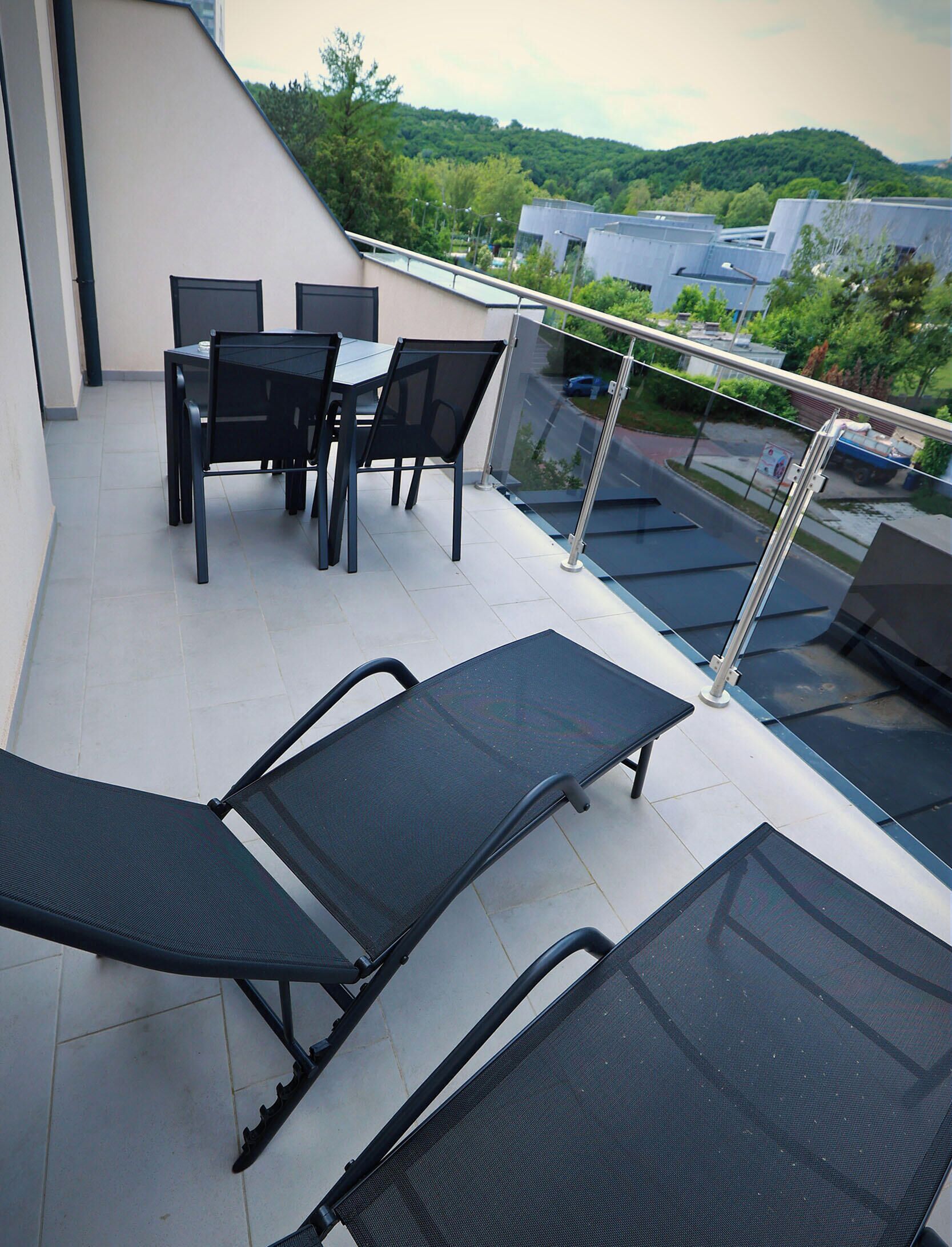 Une terrasse sur le toit, avec une table et des chaises, une balustrade en verre et une vue sur les environs.